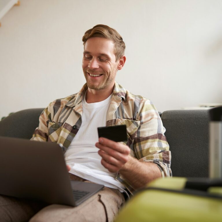 Happy man booking holiday online on laptop, paying for vacation on travel agency website, buying